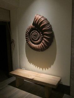 a wooden bench sitting in front of a wall with a shell on it's back