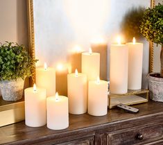 lit candles sit on a dresser in front of a mirror with potted plants next to it