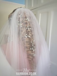 the back of a bride's head wearing a veil and hair comb with pearls on it