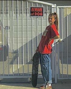 a girl holding a skateboard in front of a fenced area with a dog on it