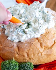 a person dipping dip into a bagel with broccoli and carrots on the side