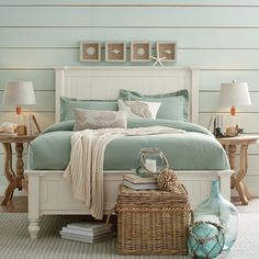 a white bed with blue sheets and pillows in a room next to two lamps on either side of the bed