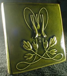 a green tile with two flowers and leaves in the center, on carpeted area