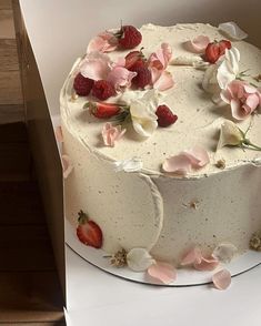 a white cake with strawberries and flowers on it sitting in a cardboard box, ready to be eaten