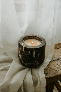 a candle sitting on top of a wooden table next to a white drapes curtain