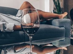 a woman laying on a couch next to a glass of wine