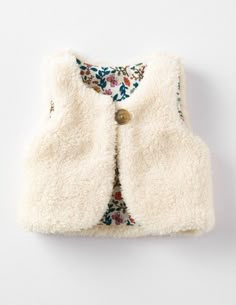 a white vest with flowers on it and a gold button in the front, hanging from a wall