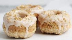 three glazed donuts with icing and sprinkles sitting on a white surface