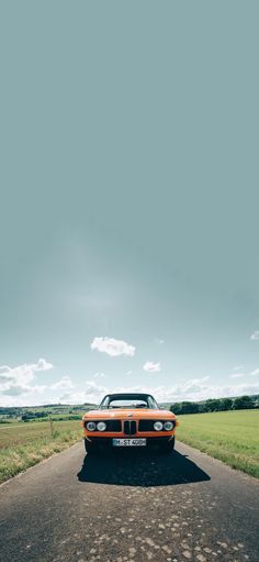 an orange and black car parked on the side of a road next to a field