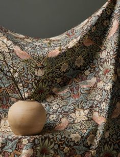 a vase sitting on top of a table covered in a fabric with flowers and leaves