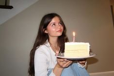 a woman holding a plate with a piece of cake on it and a lit candle in the middle