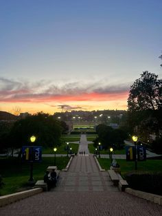 the sun is setting over a park with people sitting on benches and walking down it