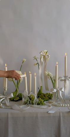 a table topped with candles and flowers next to white vases filled with green grapes