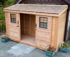 a small wooden shed with two doors and windows on the outside, surrounded by flowers