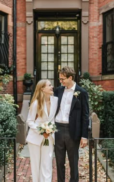 a bride and groom standing in front of a brick building with black iron railings