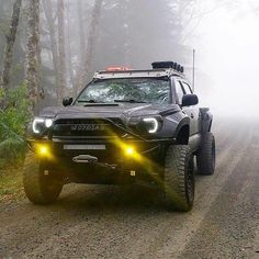 a black truck driving down a dirt road in the woods with foggy trees behind it