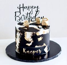 a black and gold birthday cake with happy birthday written on the top, sitting on a plate