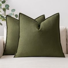 two green pillows sitting on top of a white couch next to a potted plant