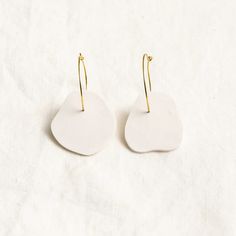 two white earrings with gold ear wires on a white surface