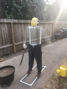 a scarecrow with a mask on standing in front of a fence holding a knife