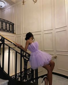 a woman in a short purple dress leaning on a stair rail with her hand on the railing