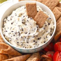 a bowl filled with cream cheese surrounded by crackers and strawberries