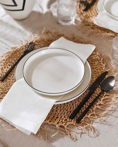 a place setting with white plates and black utensils on a burlap table cloth