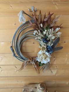 a wreath made out of rope and flowers on top of a wooden floor next to a piece of driftwood