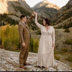 a man and woman standing on top of a mountain holding each other's hands