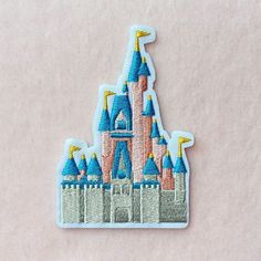 a castle embroidered onto a white surface with blue and yellow turrets on it's side