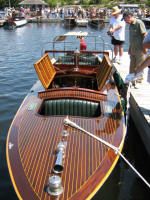 a wooden boat docked at a dock with people standing on the pier looking over it