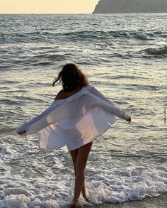 a woman is walking on the beach with her arms spread out and she is wearing a white dress