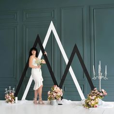 a woman in a white dress standing next to two black and white geometric shapes with flowers