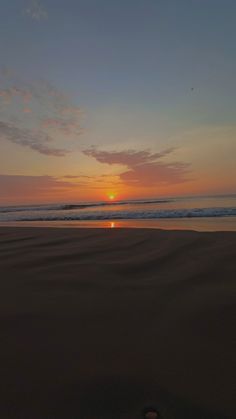 the sun is setting over the ocean and sand