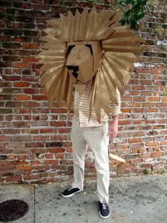 a man standing on the sidewalk with a cardboard lion mask over his face and head