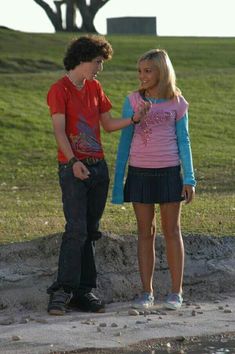 two young people standing next to each other on a field with grass and trees in the background