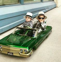 two young boys sitting on top of a green toy car