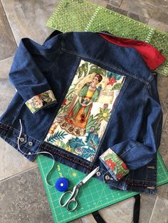 a pair of scissors sitting on top of a cutting board next to a jean jacket