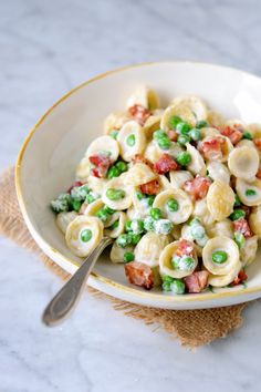 a bowl filled with pasta and peas on top of a table next to a fork