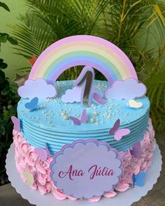 a birthday cake with blue frosting and pink flowers on the bottom, topped with a rainbow