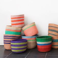 several woven baskets stacked on top of each other in different colors and patterns, against a white wall