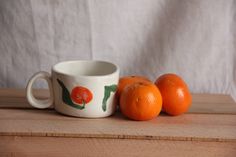 three oranges sitting next to a coffee cup on a table