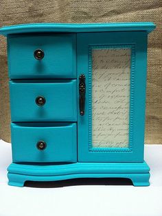 a small blue cabinet with drawers and writing paper on it's front door, sitting on a white surface