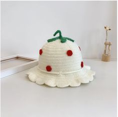 a white crocheted hat with red polka dots on the brim and green ribbon