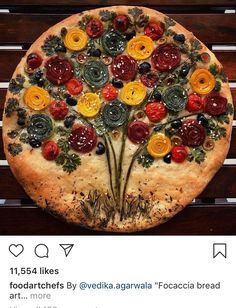 a pizza decorated with flowers and leaves on top of a wooden table next to an instagram post