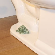 a small turtle figurine sitting on top of a white toilet seat cover next to a wooden floor