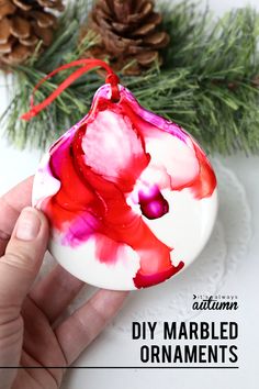 a hand holding an ornament that is painted red and white with the words diy marbled ornaments on it