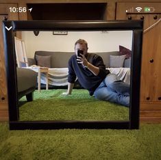 a man sitting on the floor in front of a mirror looking at his cell phone