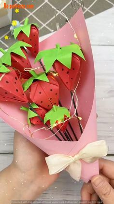 someone is holding some paper strawberries in a pink box with green leaves on it