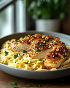 a white bowl filled with pasta and chicken on top of a wooden table next to a potted plant